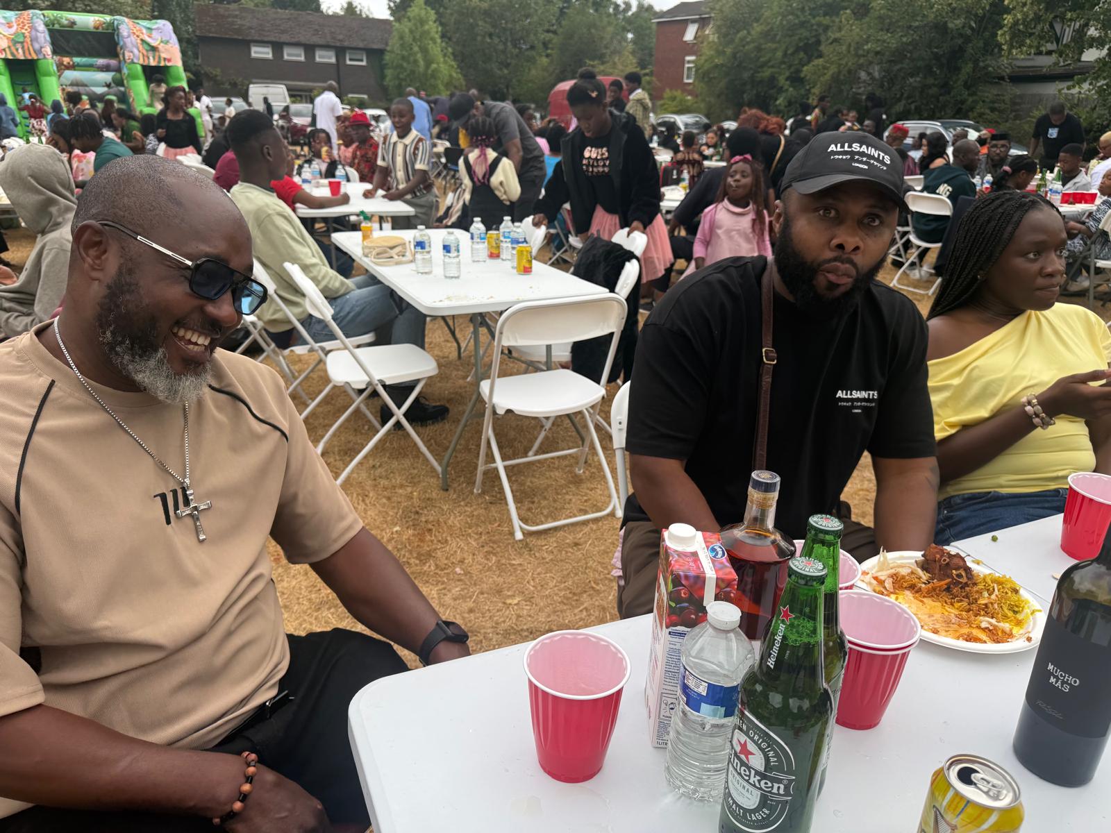 Members laughing together at a table during the AUF family fun day, with bouncy castles behind